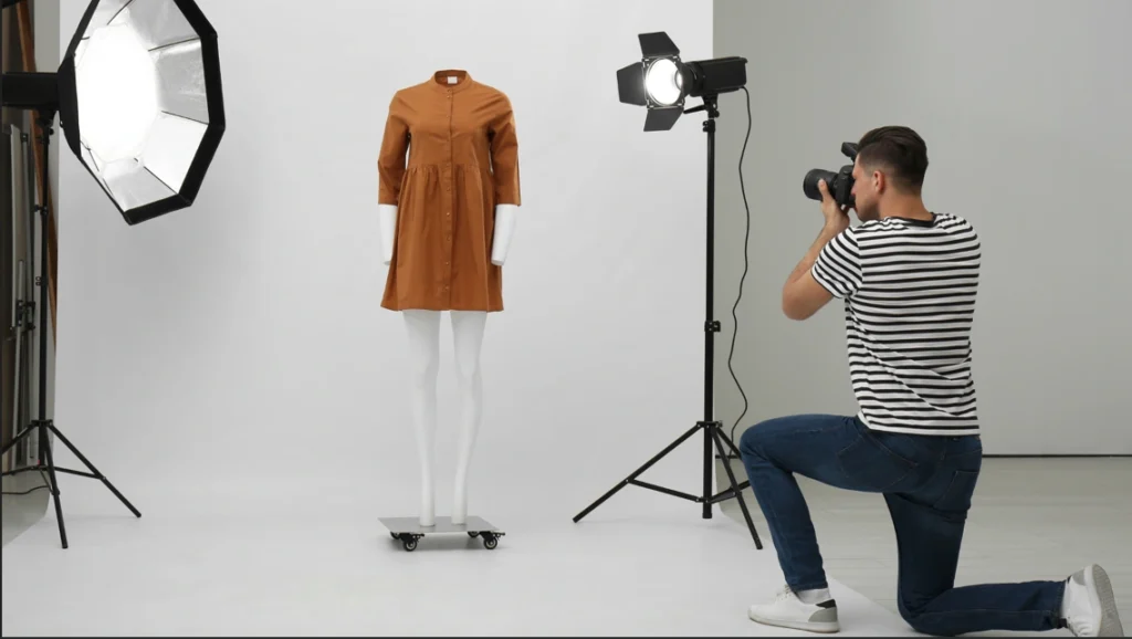 How to Ghost Mannequin Photography A male photographer, wearing a striped shirt and jeans, kneels on the floor to take a picture with a DSLR camera